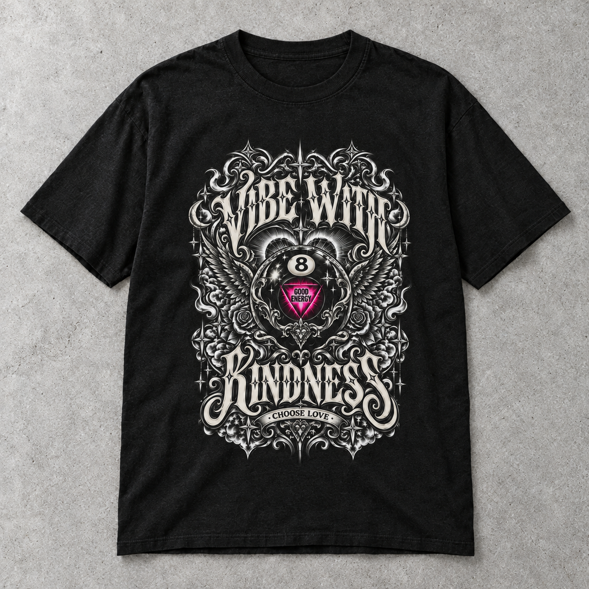 Black Vibe With Kindness ornate 8-ball graphic tee laid flat on a gray textured background.