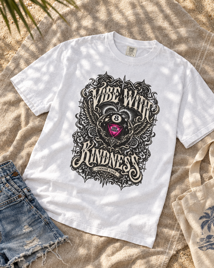 White Vibe With Kindness ornate 8-ball graphic tee laid flat beside denim shorts on a textured surface.