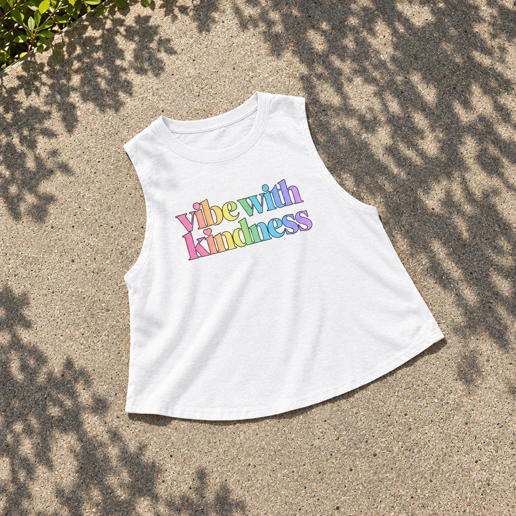 AI-generated styled flatlay of the white Vibe With Kindness rainbow crop top on concrete.