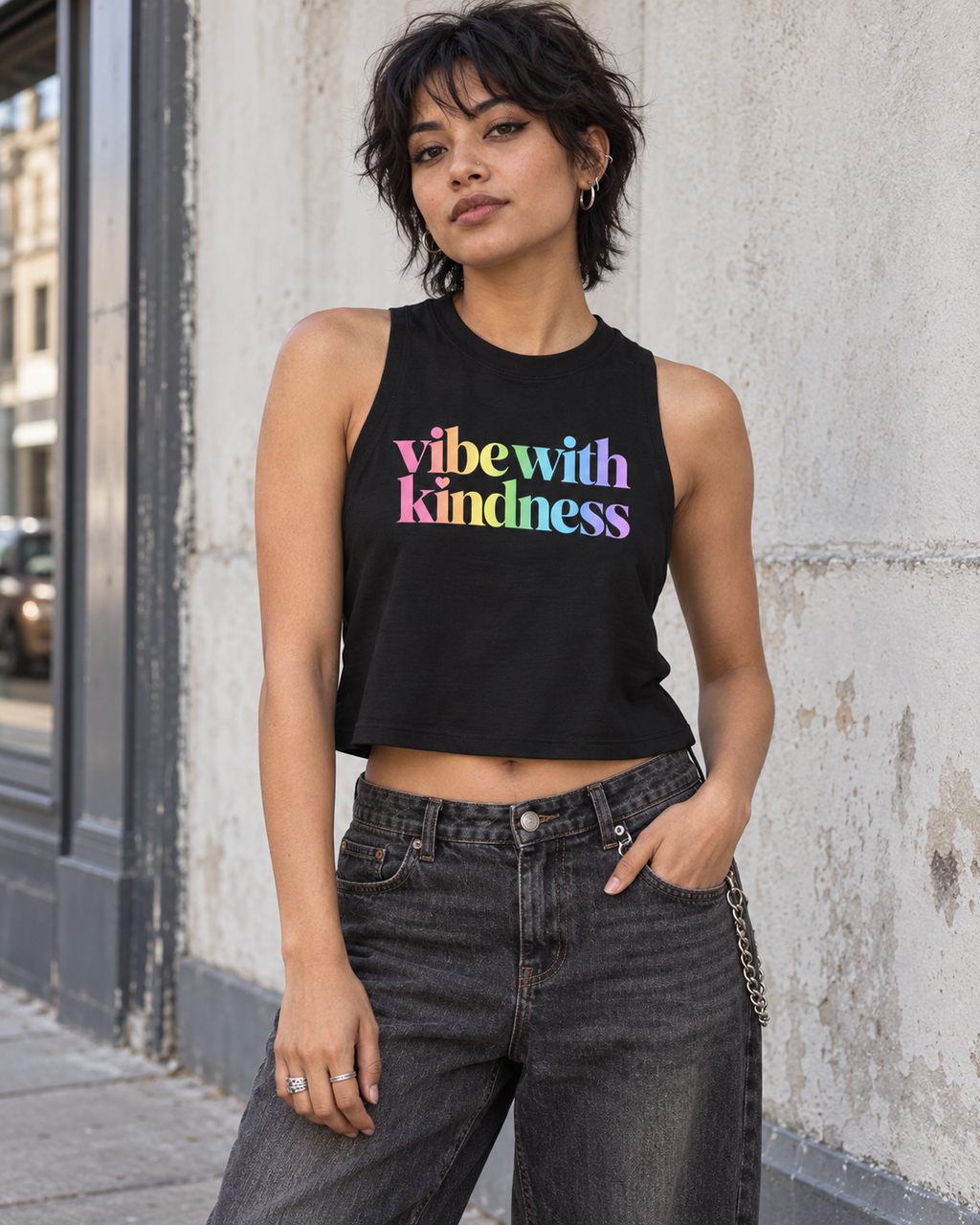AI-generated styling mockup of the black Vibe With Kindness racerback crop with rainbow logo, standing urban outfit.