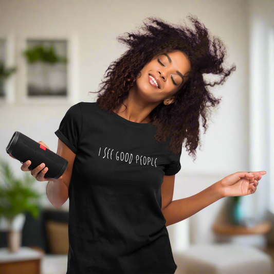 A studio mockup of a woman enjoying music while wearing a black 'I See Good People' t-shirt. The minimalist white text design on the garment-dyed fabric pairs perfectly with her relaxed and joyful vibe, showcasing the t-shirt's comfortable fit and positivity-focused message.