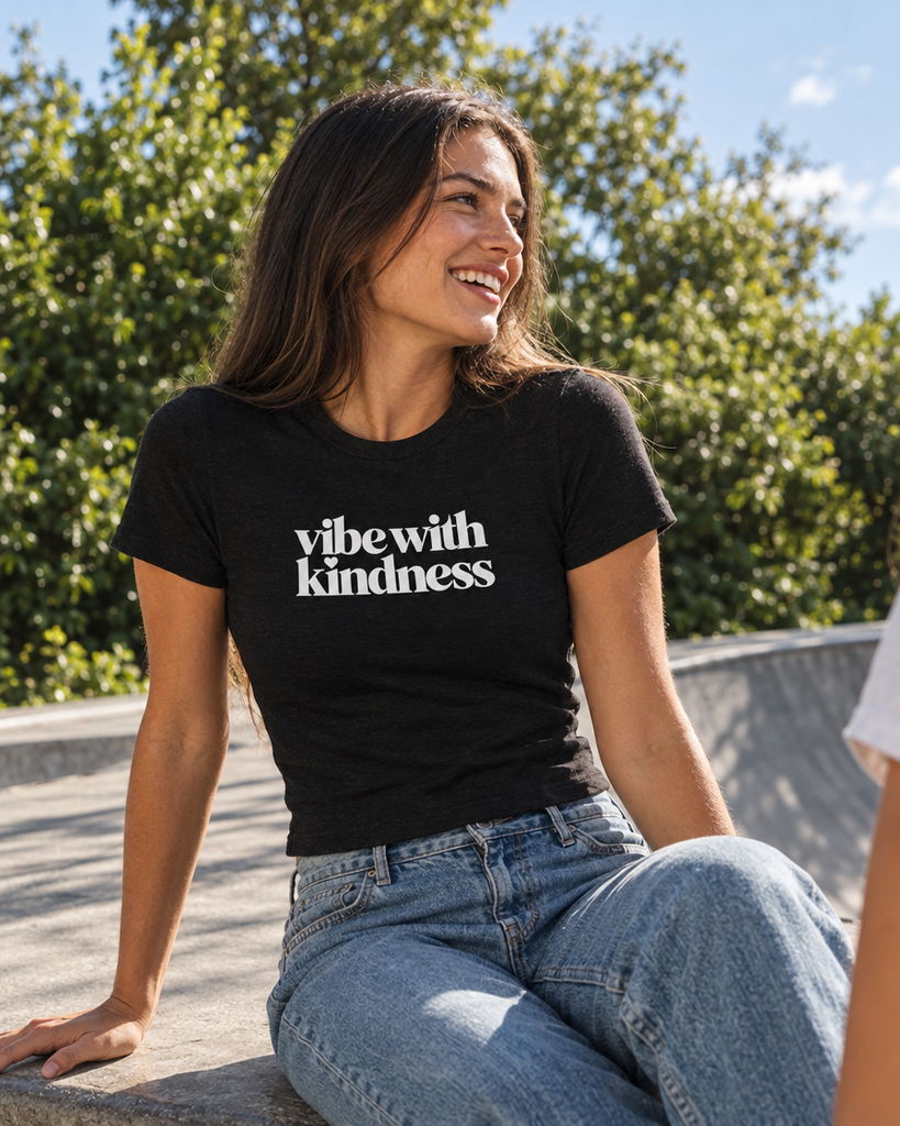 Black fitted Vibe With Kindness tee with white chest wordmark, styled with denim outdoors — AI lifestyle mockup